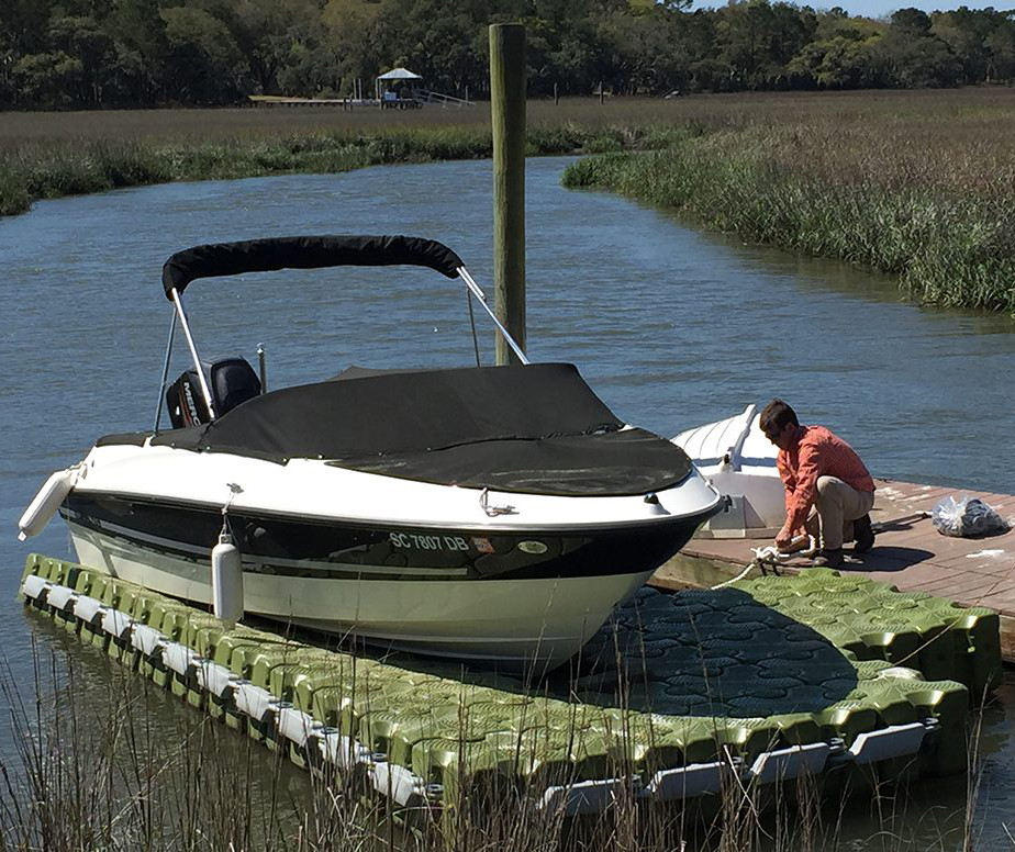 A man ties his boat down on a green floating dock.