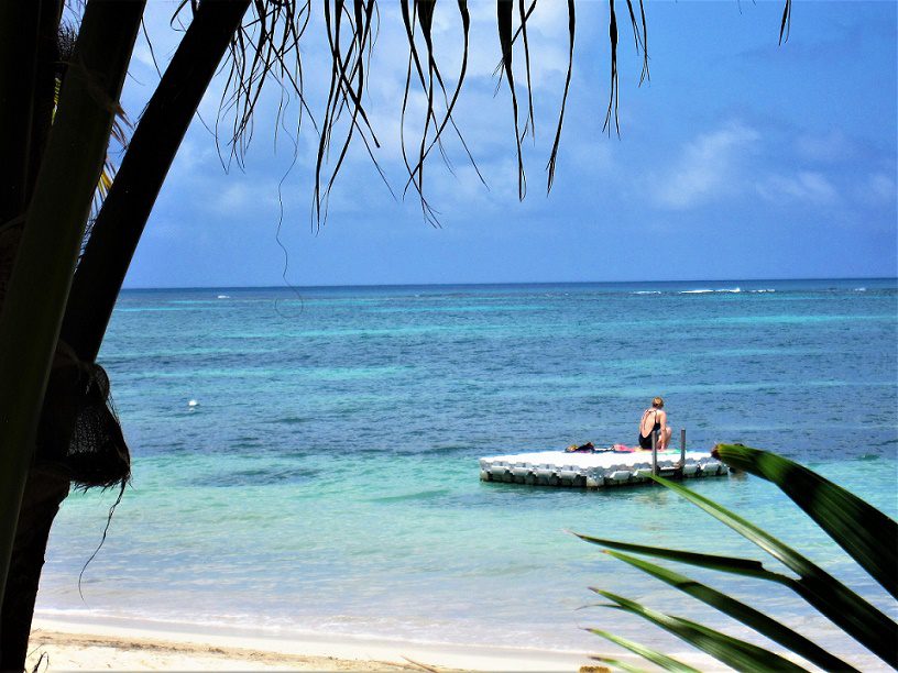 A woman in a swimsuit sits on a floating dock in a tropical paradise.
