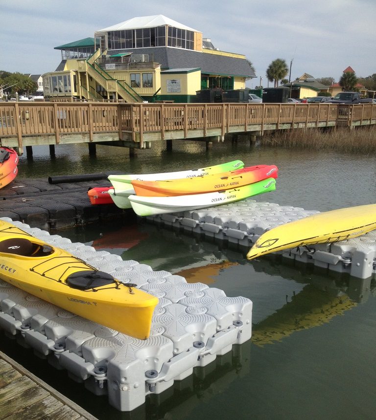 A pile of kayaks sit on top of a floating dock.