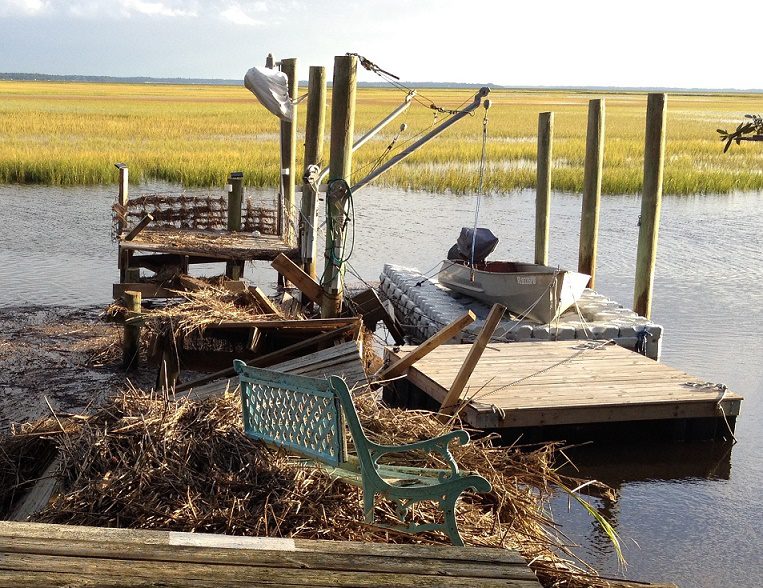 A torn up wooden dock after a hurricane is next to a completey untouched modular Dock Blocks dock, with a small fishing boat atop it.