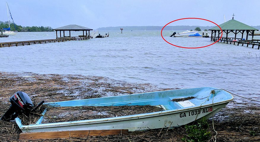 A boat swept to shore after a hurricane, but in the background, a boat sits on it's floating dock unscathed.