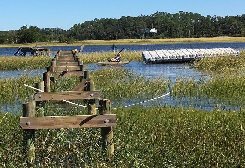 A person kayaks on a lake while tugging a custom floating dock to a new location.