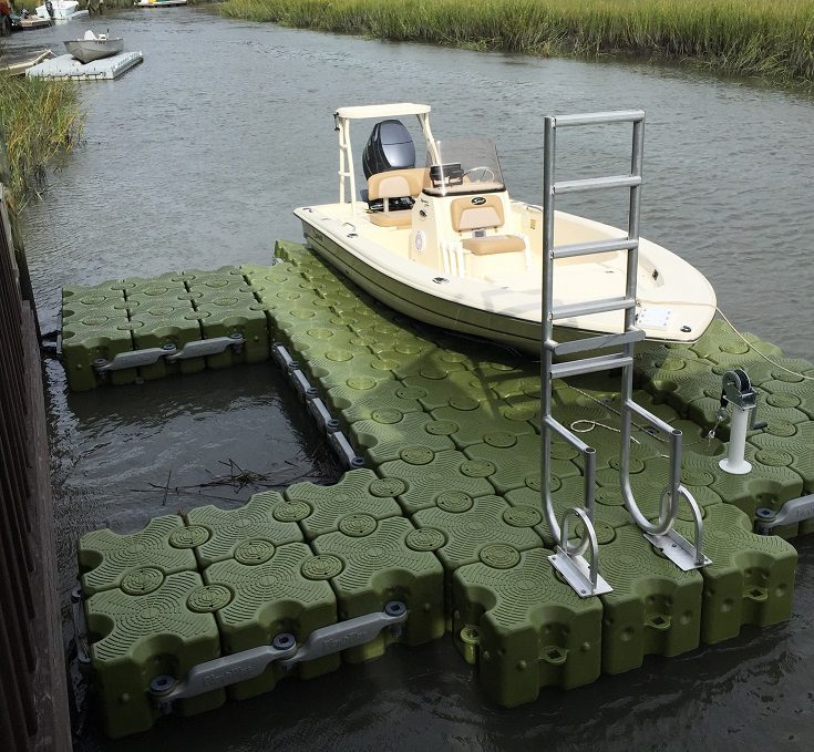 A small fishing boat sits on top a modular green floating dock, unmanned.