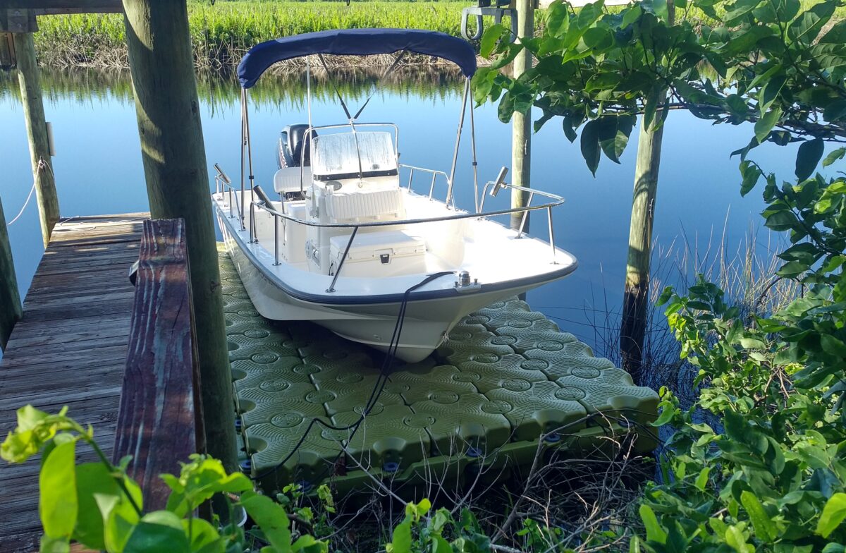 A small fishing boat sits on a green floating dock in a marshy area.