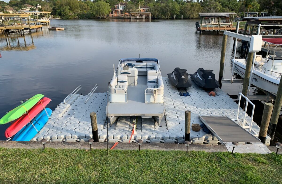 A pontoon boat and kayaks sitting on a floating dock.