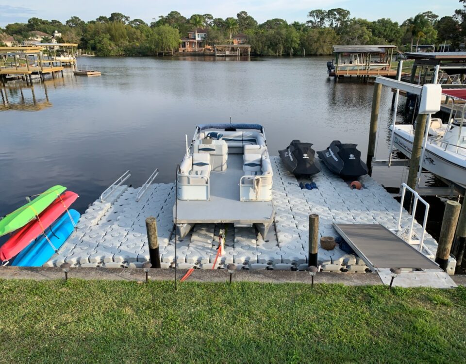 A pontoon boat and kayaks sitting on a floating dock.